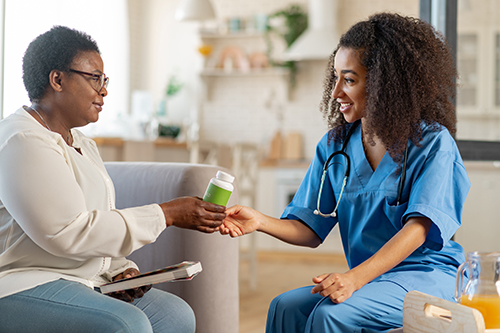 Young nurse handing elderly woman a bottle of vitamins