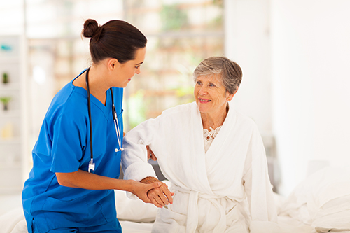 Nurse in blue scrubs helping elderly woman stand up