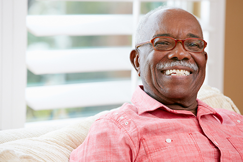 Man with mustache and glasses smiling at camera wearing a red shirt