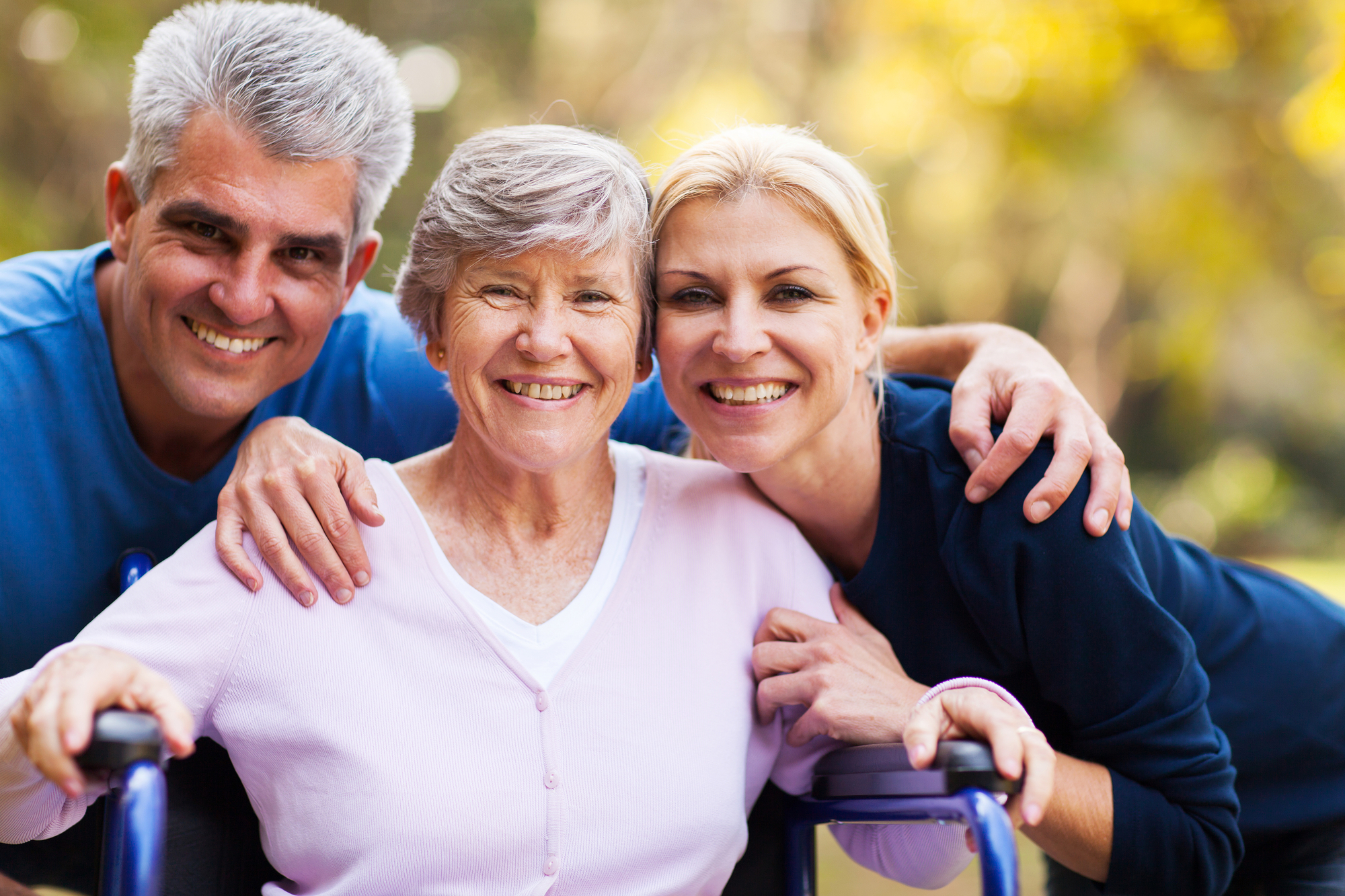 mother in purple sweater in wheelchair with daughter and son crouched down smiling on each side of her in blue